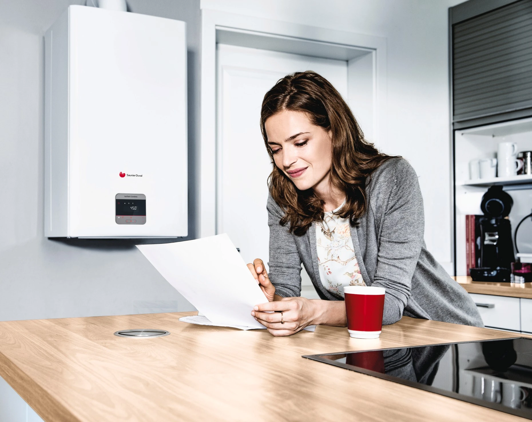 kobieta przygląda się rachunkowi za ogrzewanie na tle kotła gazowego zainstalowanwgo w kuchni